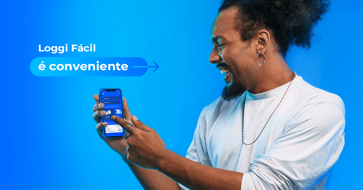 Um homem preto, com o cabelo amarrado e vestindo uma blusa branca, sorri enquanto segura um celular que mostra a tela inicial do Loggi Fácil, o serviço de envios da Loggi.