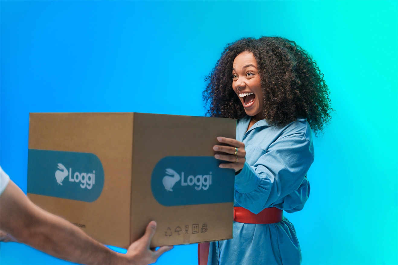 Moça recebendo pacote da Loggi com fundo azul
