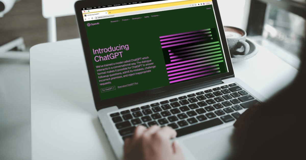 A imagem mostra um notebook em uma pessoa, enquanto um homem acessa a home page do ChatGPT. O homem não aparece na imagem, apenas sua mão e parte do ombro.